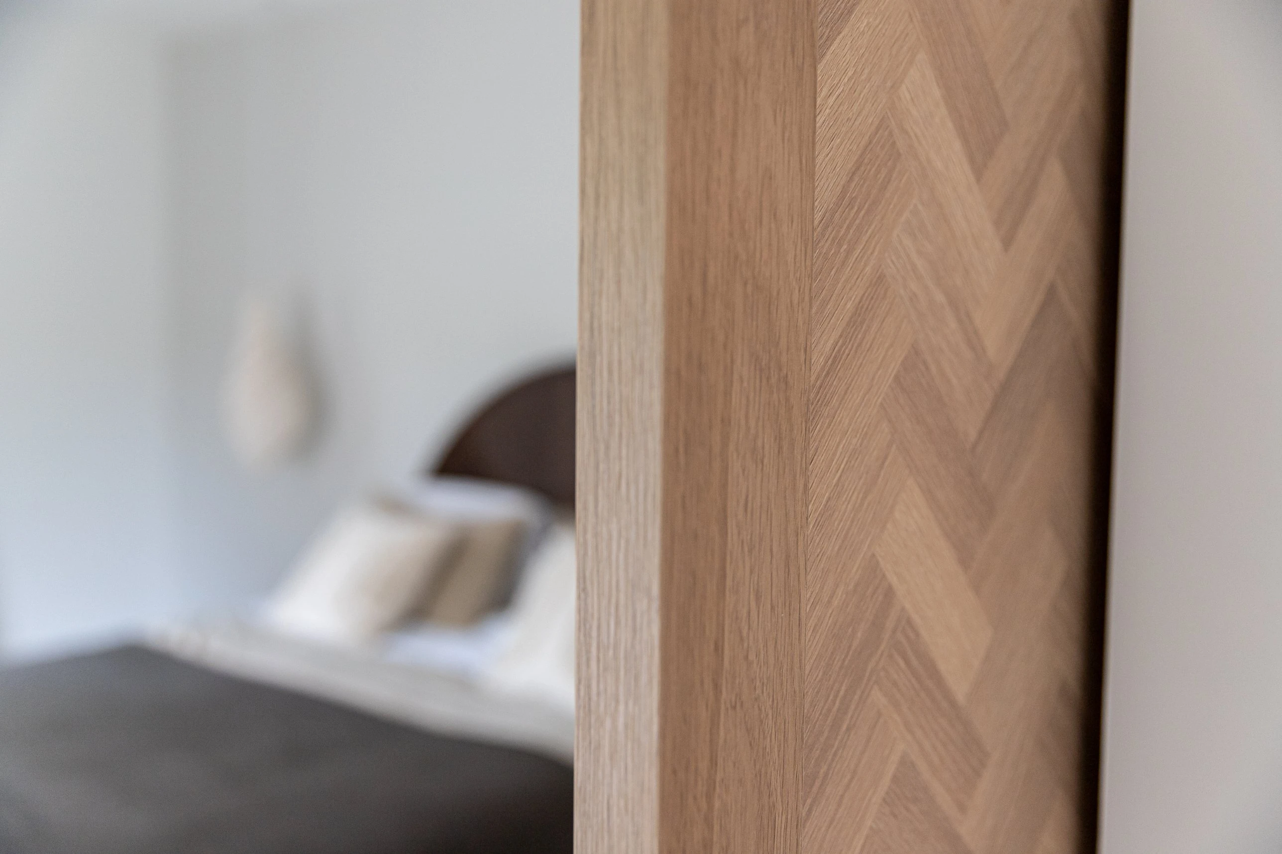 Detail van een eikenhouten deur met visgraatpatroon, met een slaapkamer op de achtergrond