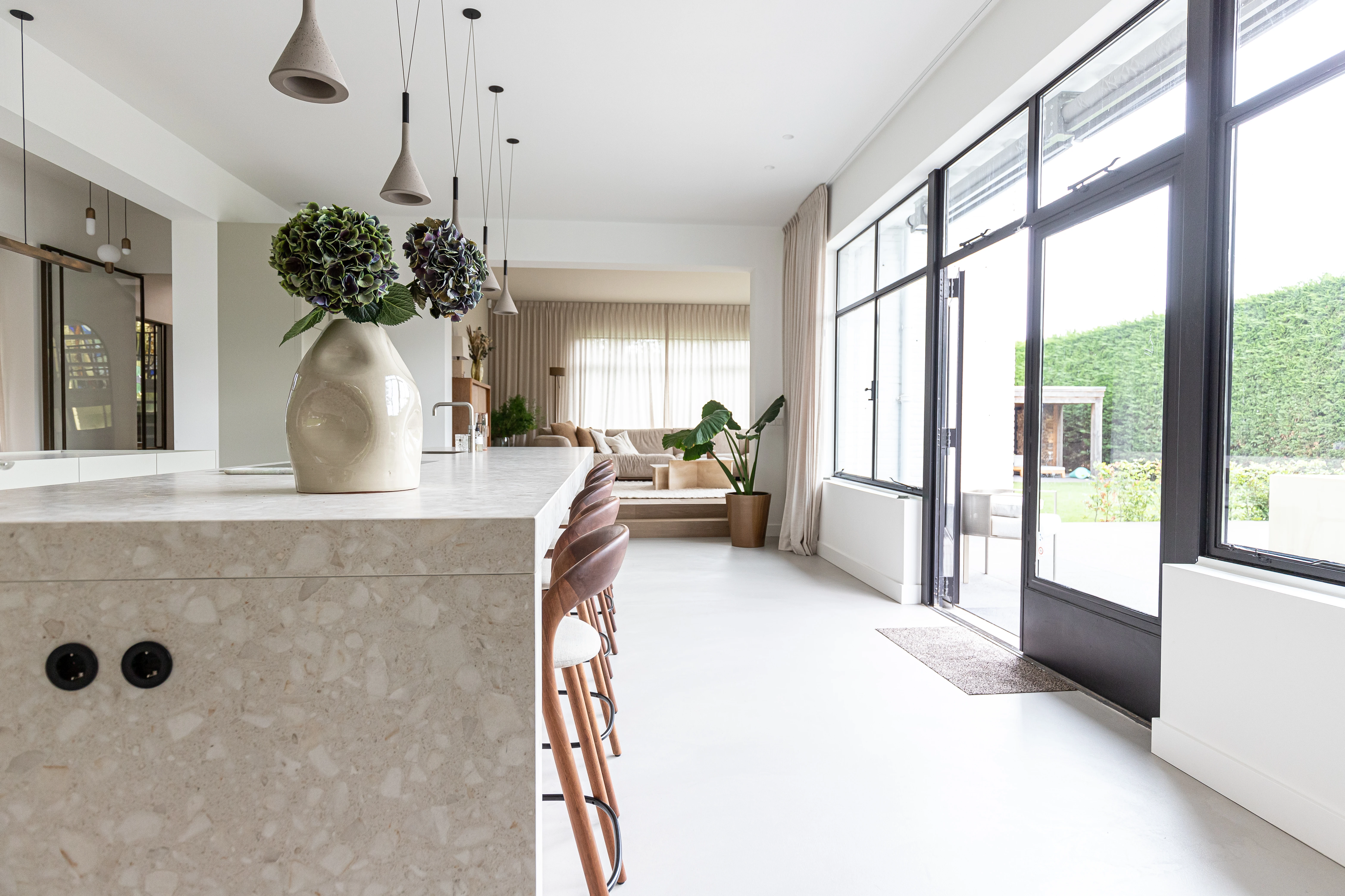 Terrazzo keukenblad met inbouwcontactdozen, hanglampen en een zwarte stalen tuindeur naar de tuin