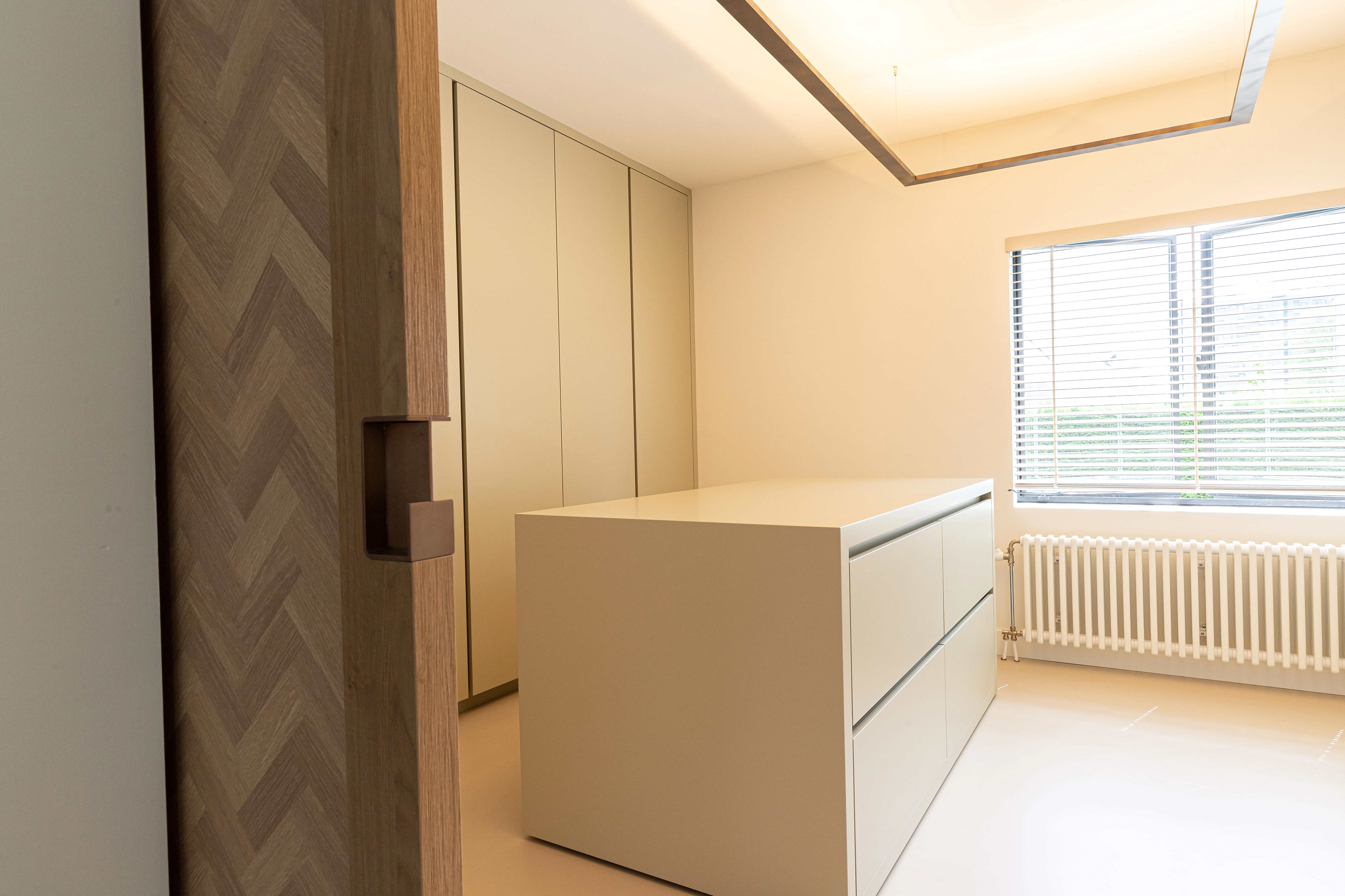 Kleedkamer met een kasteneiland en een kastenwand, gezien langs een eikenhouten visgraatdeur