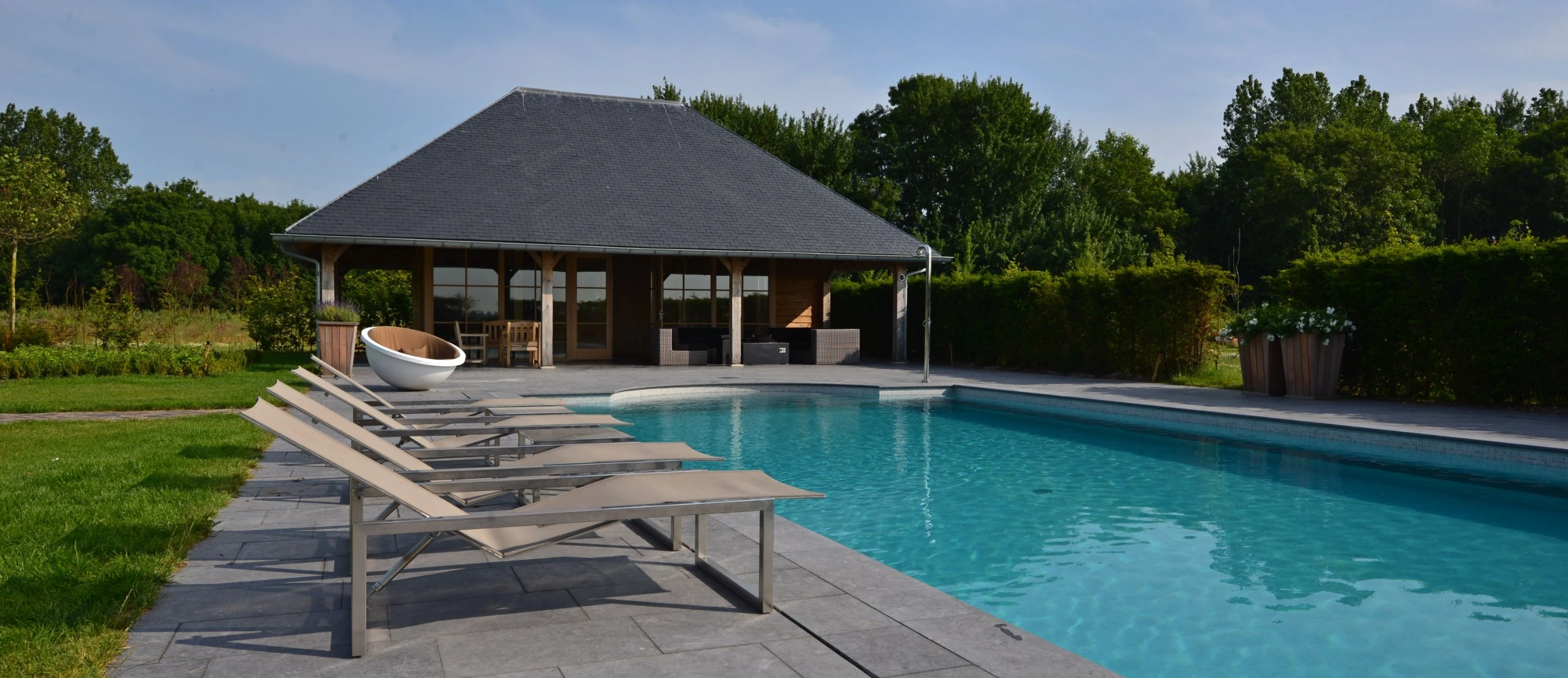 Poolhouse met eikenhouten spanten aan het zwembad, met ligbedden op een leistenen terras