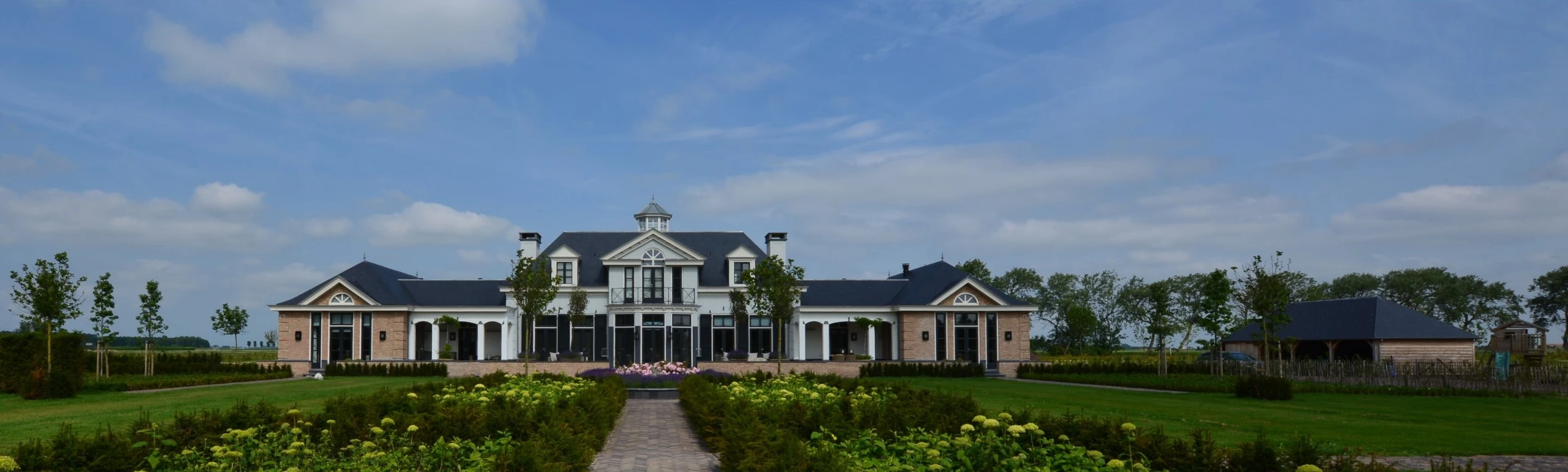 Brede opname van de villa in Sommelsdijk met symmetrische vleugels onder een heldere lucht