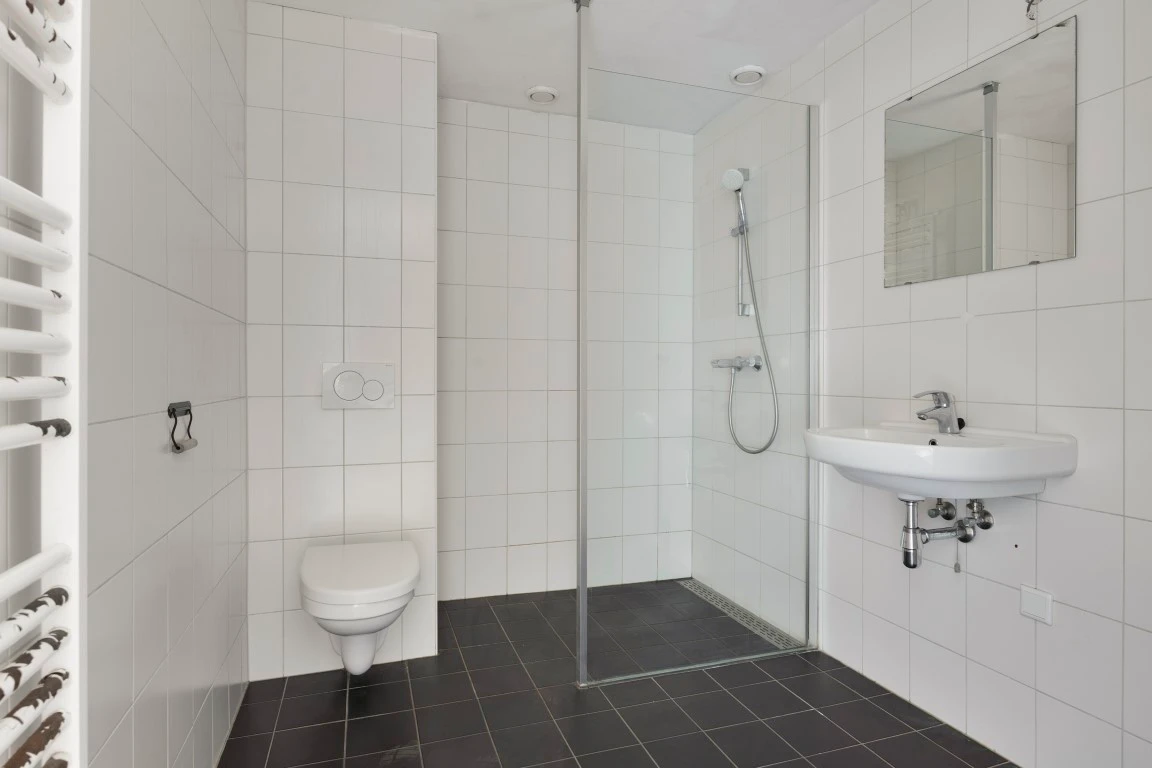 Kleine badkamer met witte wandtegels, een inloopdouche, een hangend toilet en een handdoekradiator