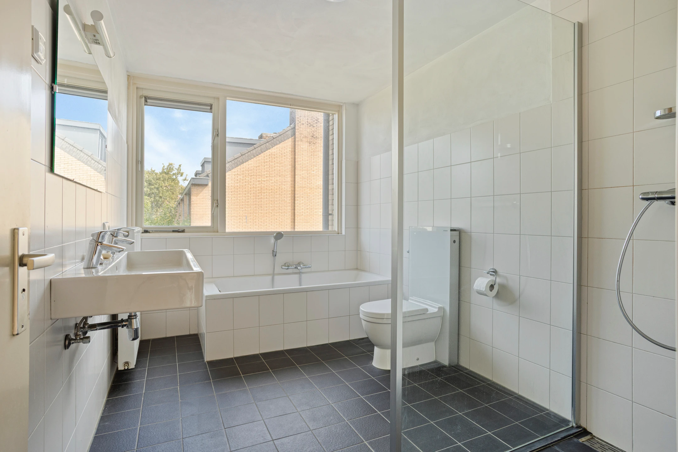 Badkamer met witte wandtegels, een ligbad, een wastafel en een inloopdouche