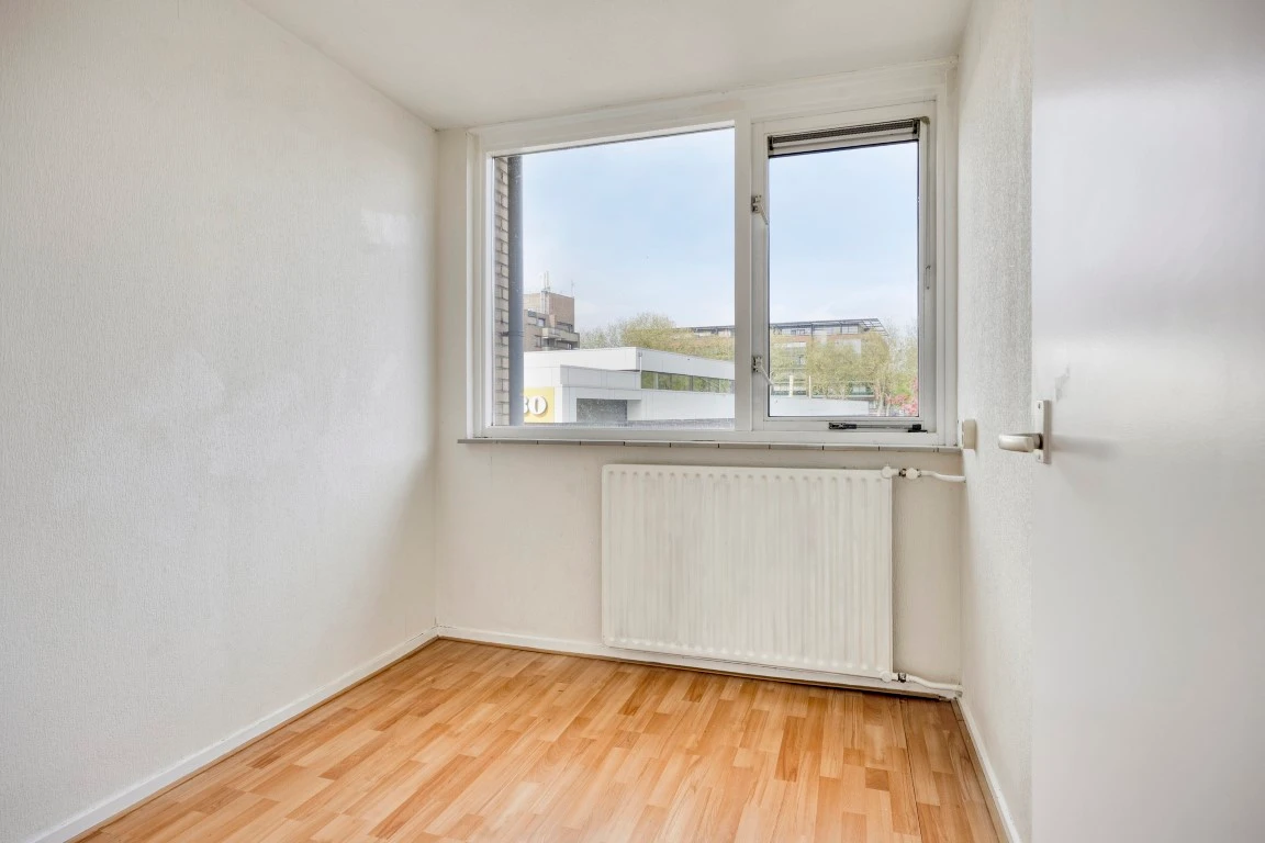 Kleine lege kamer met een raam, een radiator en een laminaatvloer