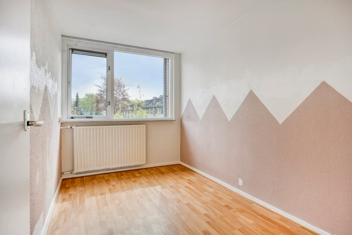 Lege kamer met een roze driehoekenpatroon op de wand, een raam en een laminaatvloer