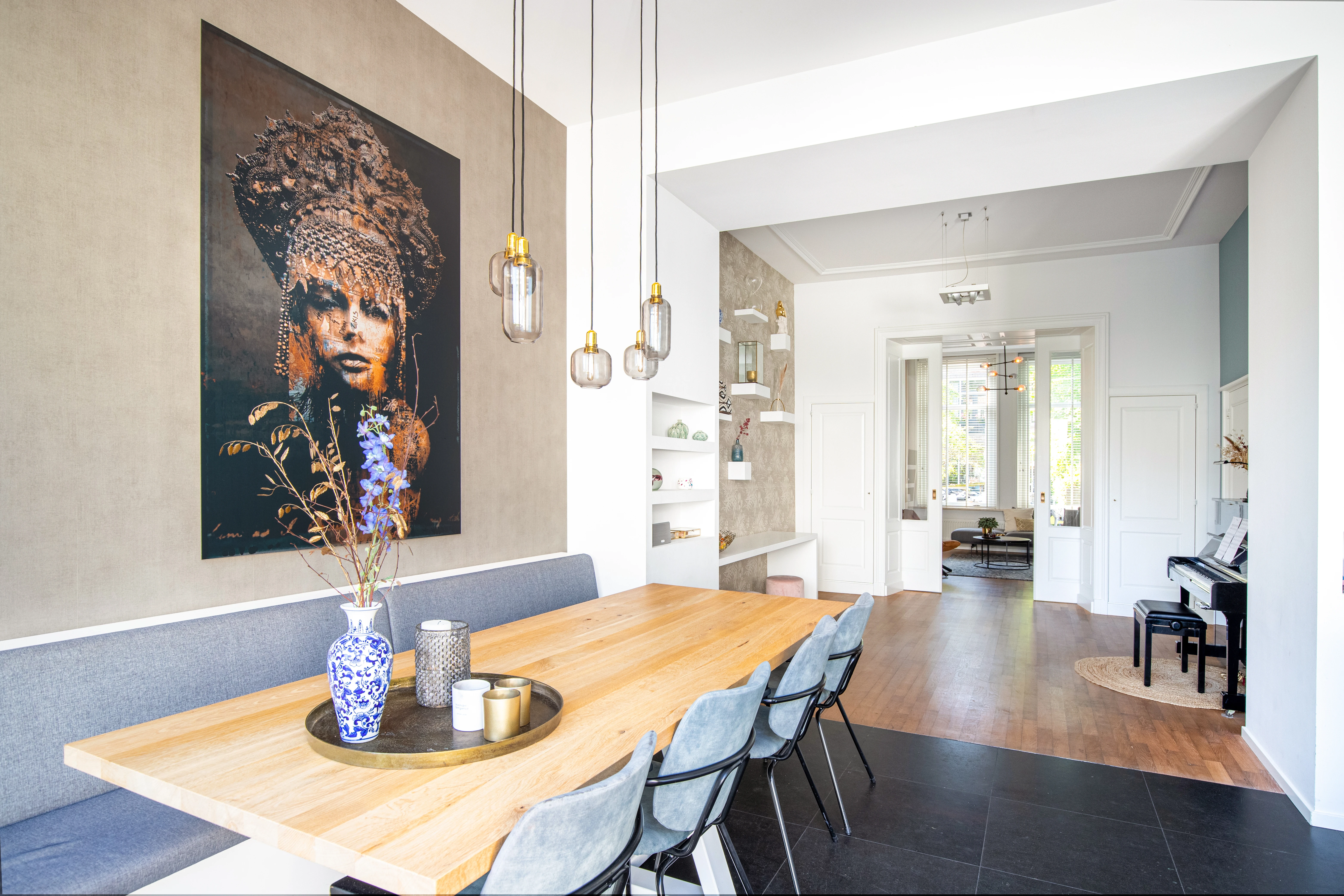 Eetkamer met een groot portret aan de wand en hanglampen boven de eettafel