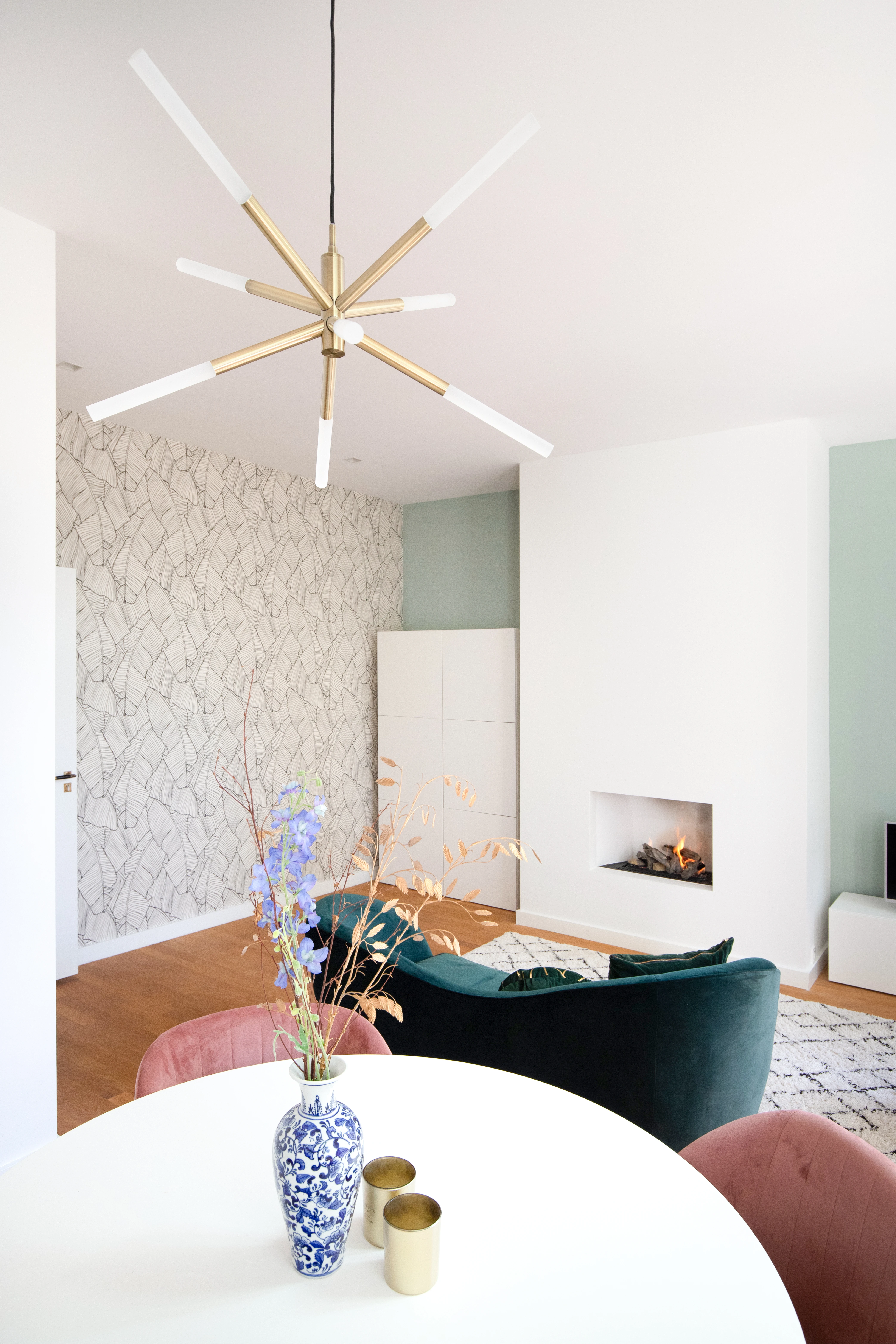 Woonkamer met een groenfluwelen bank en een ronde eettafel met roze stoelen