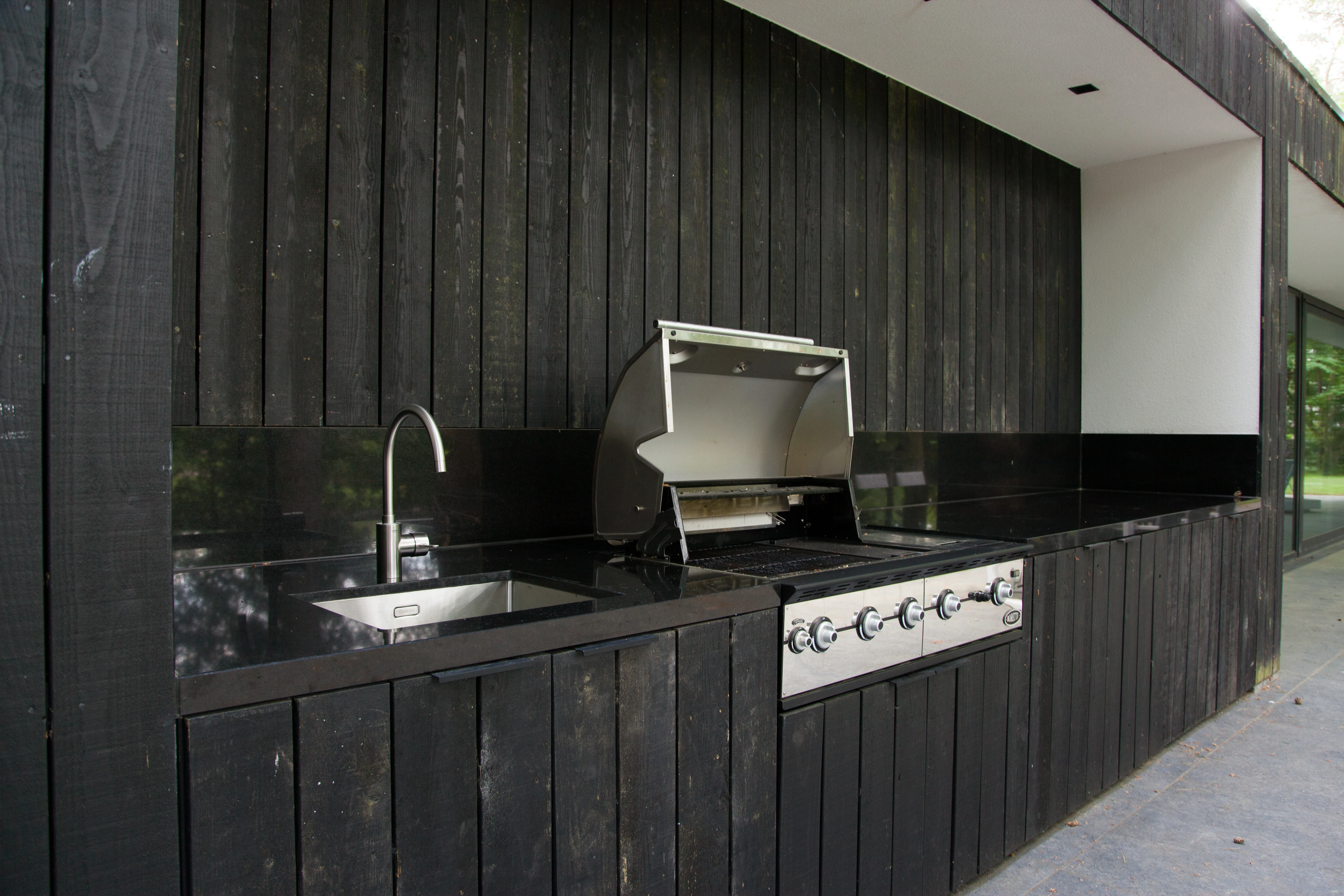 Buitenkeuken met zwart gevelhout, een spoelbak, kraan en een gasbarbecue
