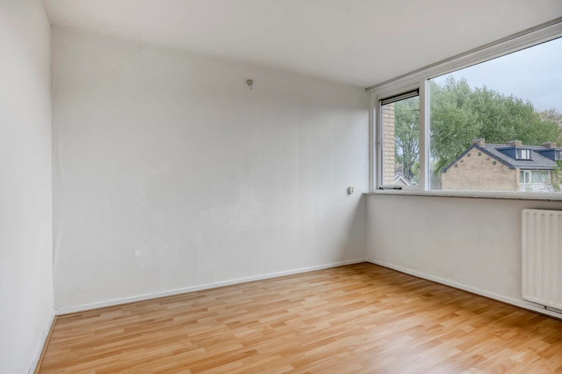 Lege slaapkamer met witte wanden, een raam over de hoek en een laminaatvloer